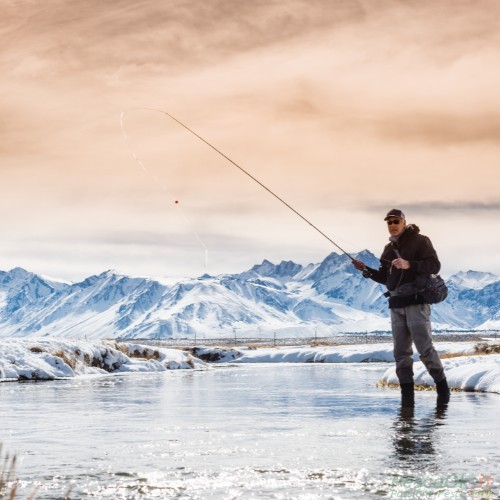 Pescatore in riva ad uno specchio d'acqua circondato da un paesaggio invernale